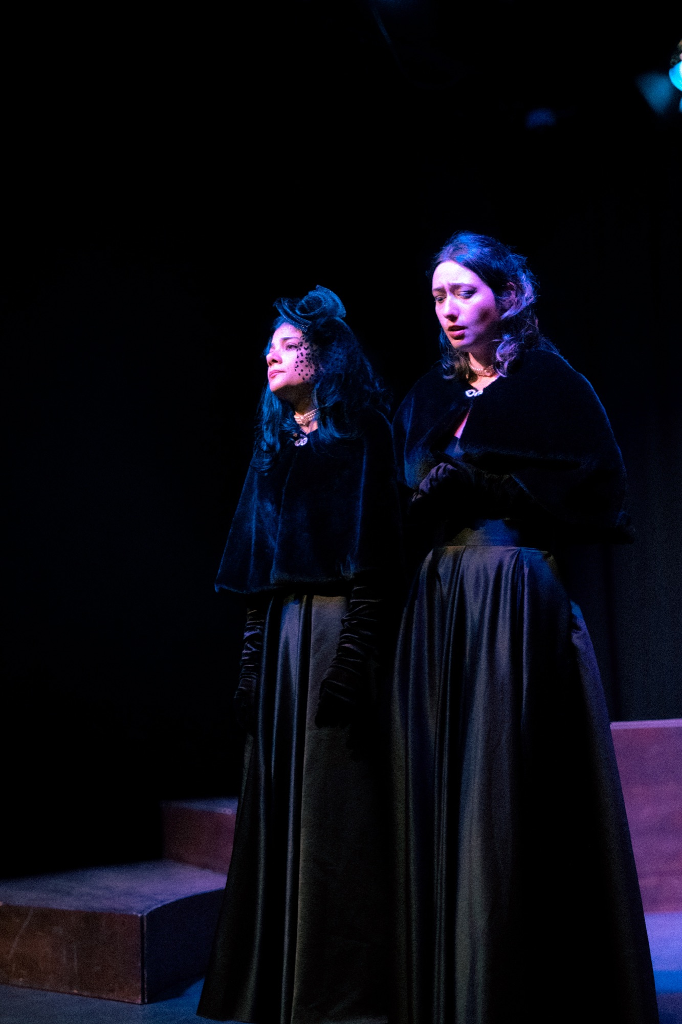 Two performers in black Victorian dresses on stage
